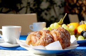 A croissant on a plate with a cup and a bowl of fruit.