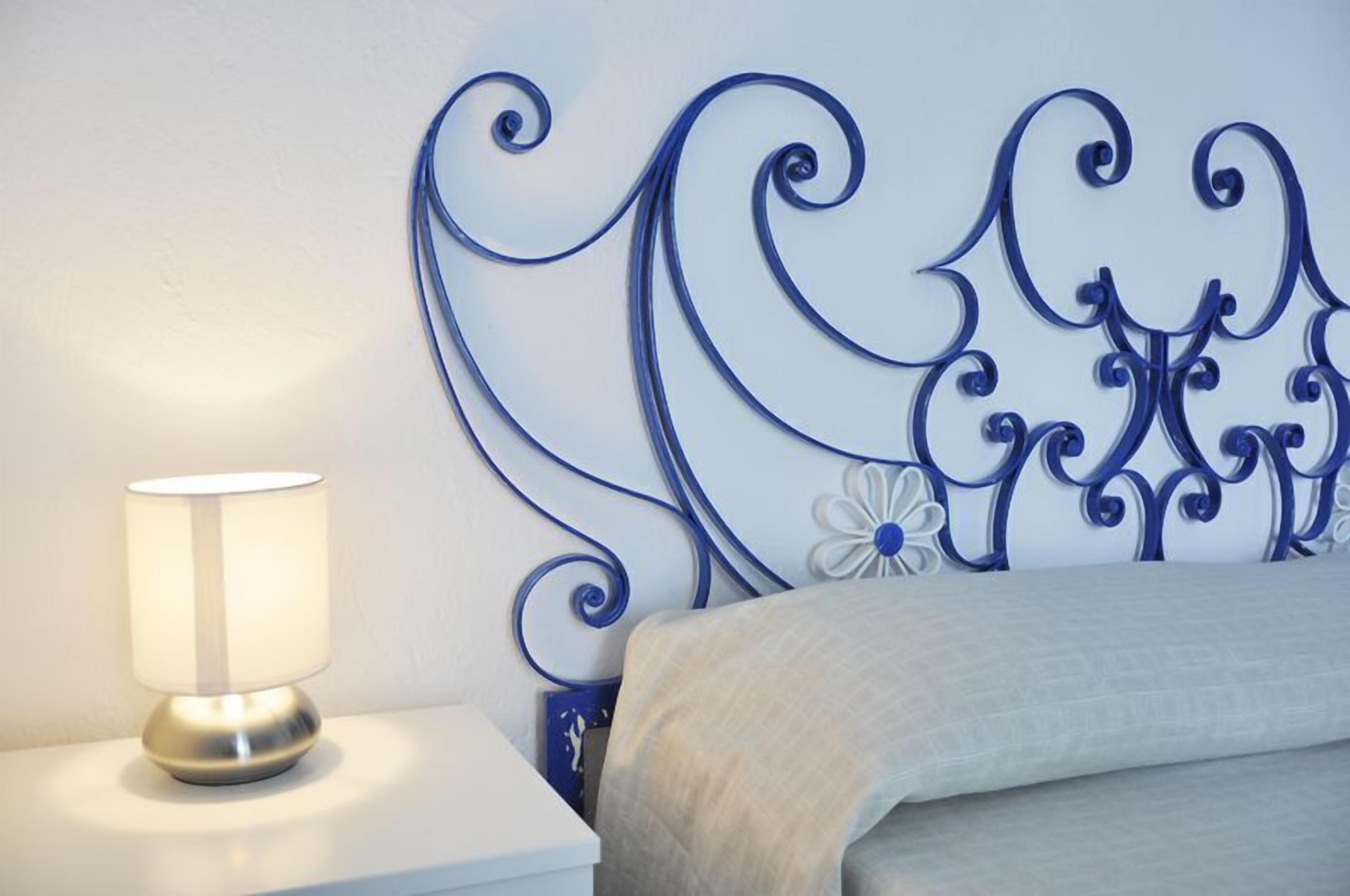 Una cama con cabecera decorativa, una lámpara de noche y una mesita.