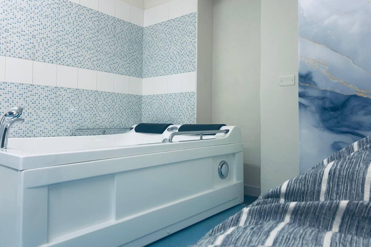 A bathroom with a white bathtub, a shower, and a tiled wall with a blue pattern.