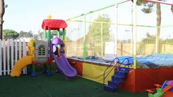 Une aire de jeux avec un toboggan, des structures d’escalade et un espace de jeux sécurisé par un filet.