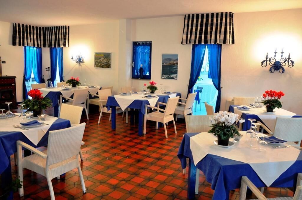 A dining area with tables set for two, blue tablecloths, white chairs, and blue curtains.
