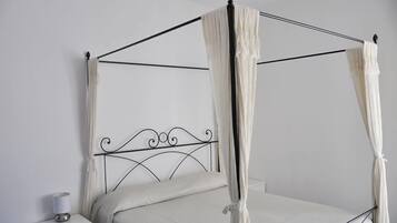 Un lit à baldaquin avec des poteaux et un ciel de lit blancs, une table de chevet avec une lampe, et un mur blanc uni.
