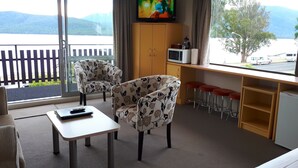 A room with two floral armchairs, a small table, a TV, a microwave, and a view of a lake and mountains. - Edgewater Motel Te Anau (Te Anau)