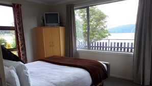 A hotel room with a bed, a television on a cabinet, and a window with a view of trees and a fence. - Edgewater Motel Te Anau (Te Anau)