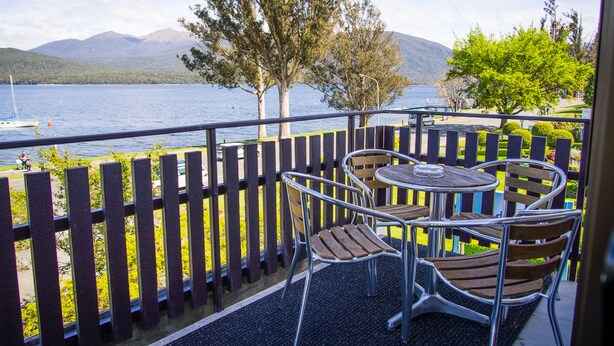A balcony with a table and chairs overlooking a lake with mountains in the background. - Edgewater Motel Te Anau (Te Anau)
