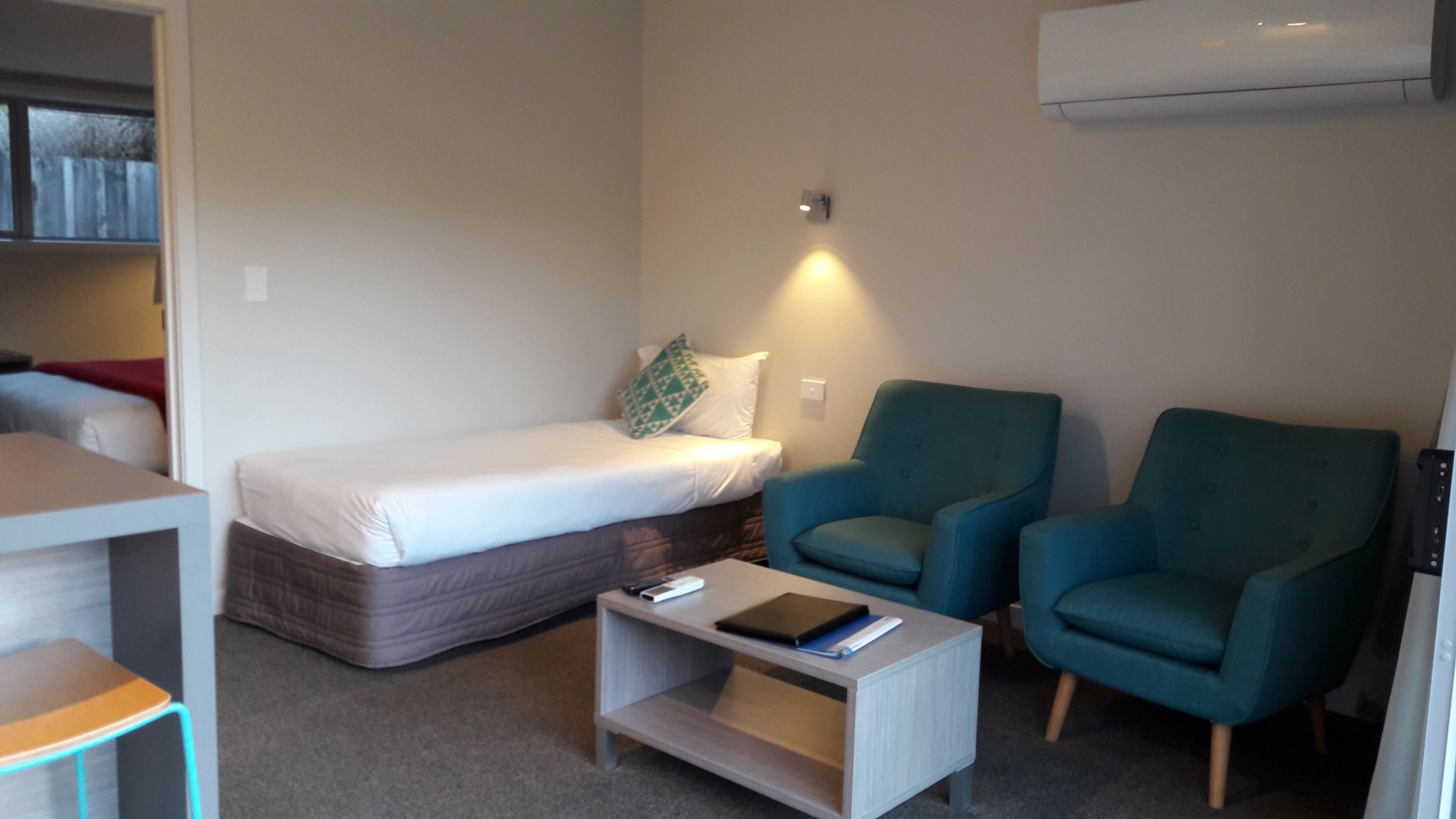 A compact room with a single bed, two armchairs, a small table, and a wall-mounted air conditioner.