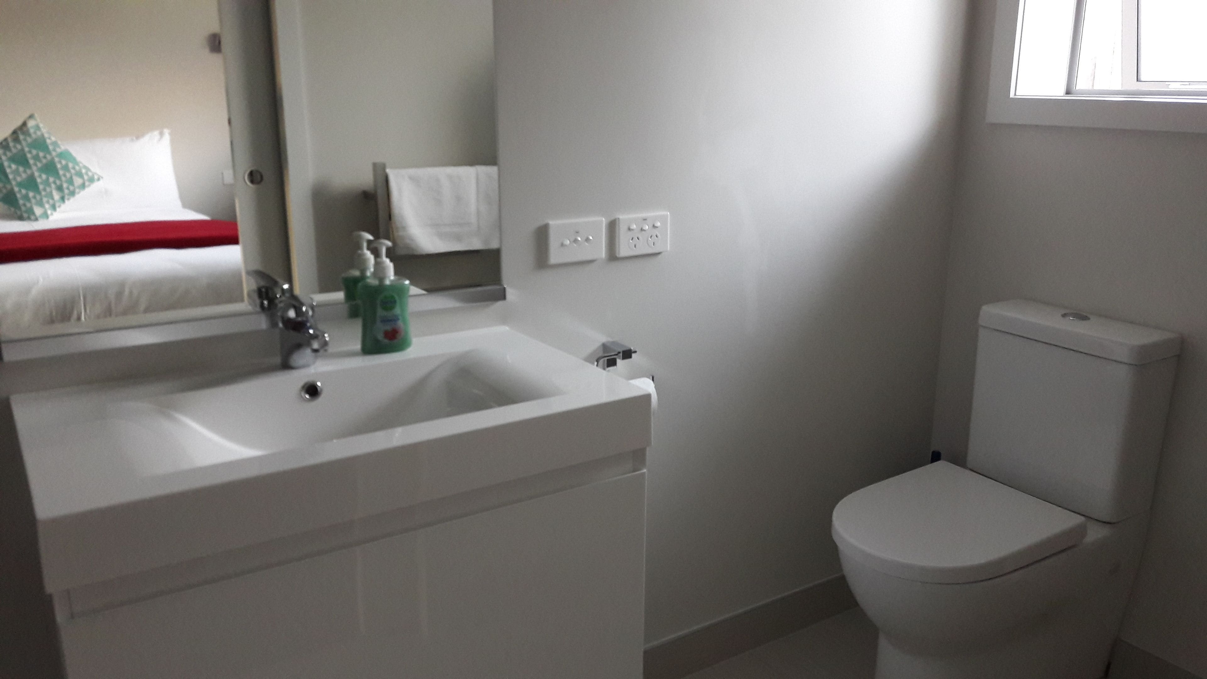 Et badeværelse med et hvidt håndvask, et spejl, et toilet og et vindue.