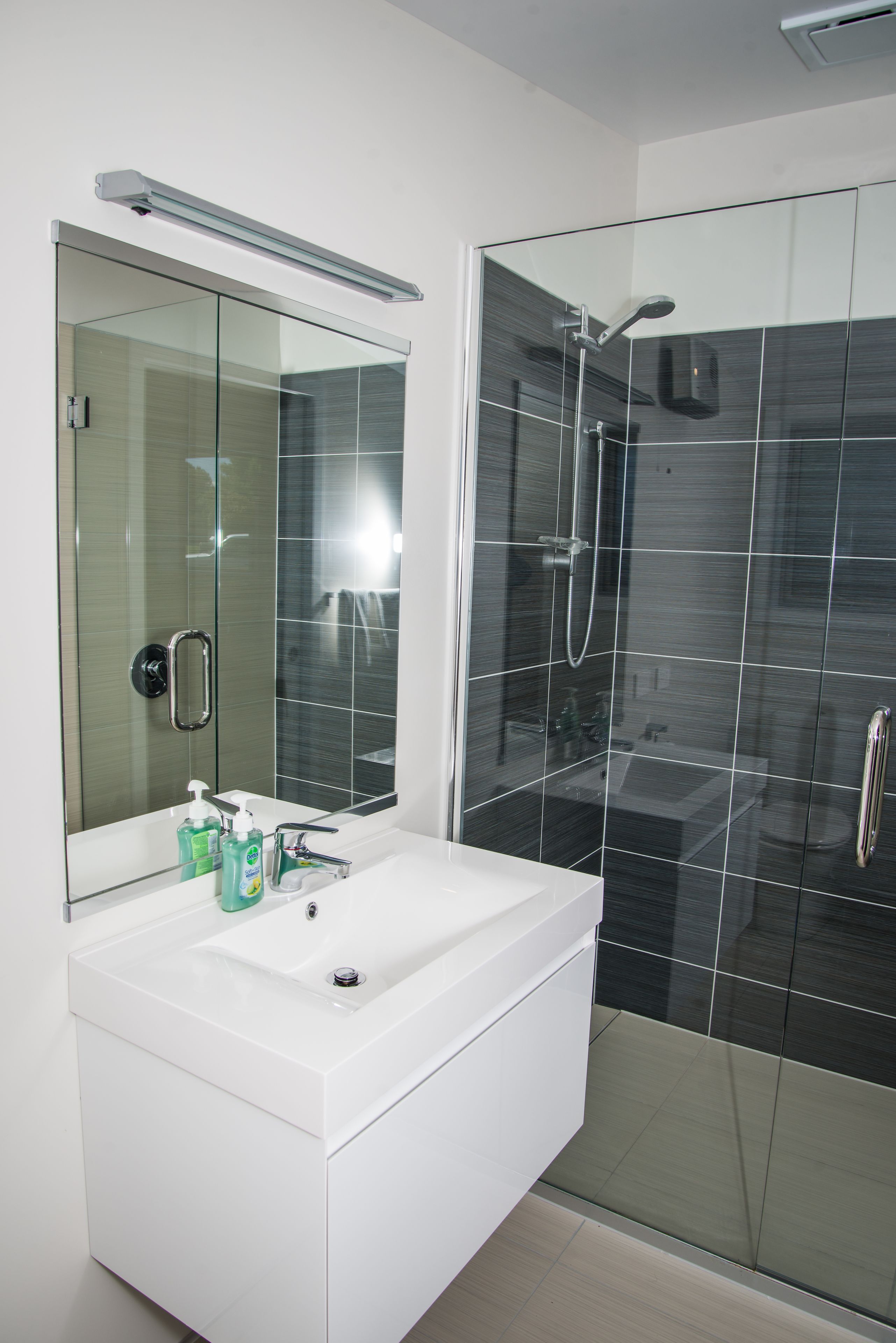 A modern bathroom with a glass-enclosed shower, a white sink with a mirror, and toiletries on the counter.