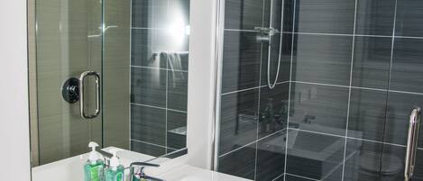 A modern bathroom with a glass-enclosed shower, a white sink with a mirror, and toiletries on the counter.