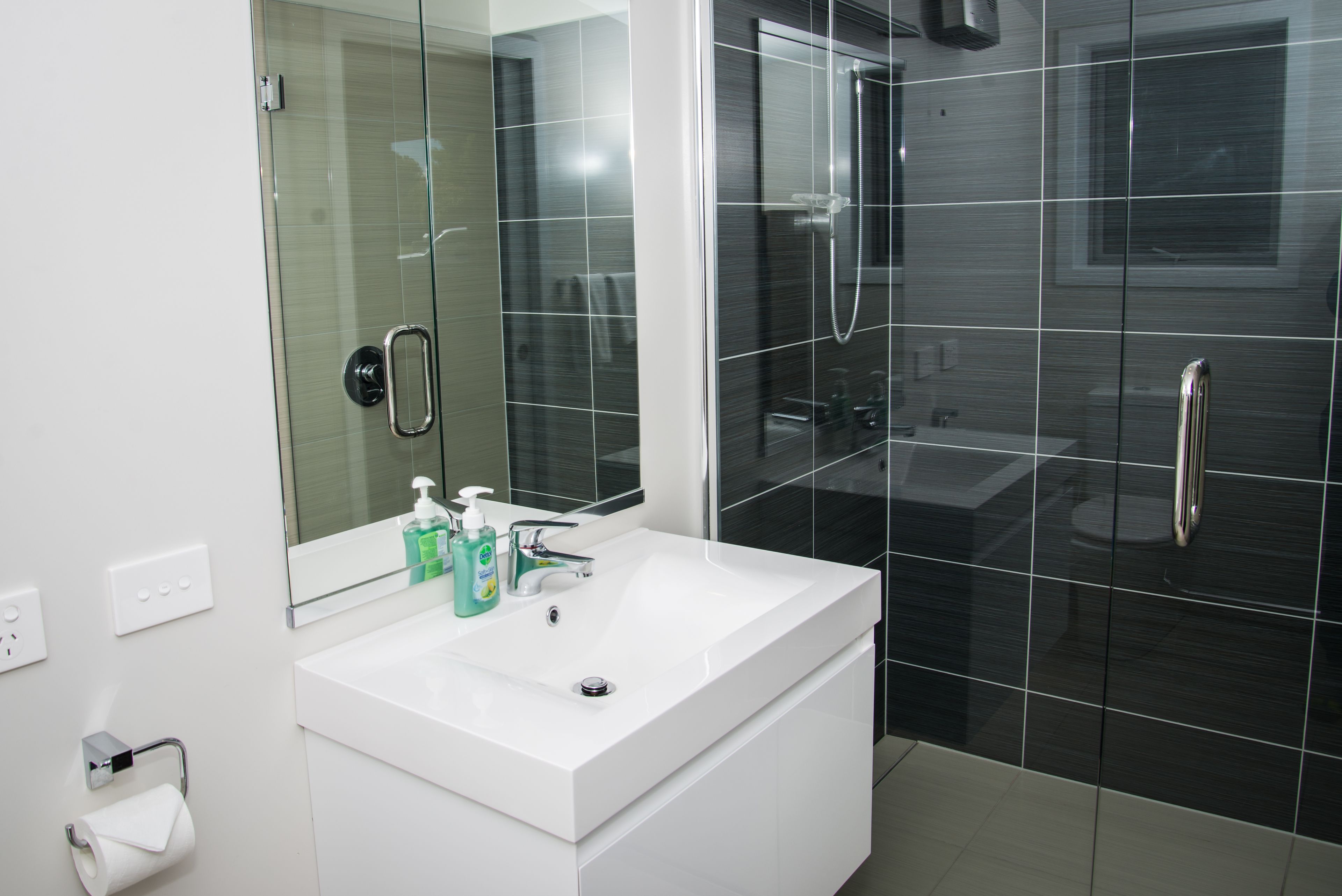 A modern bathroom with a white sink, a large mirror, and a glass-enclosed shower area.