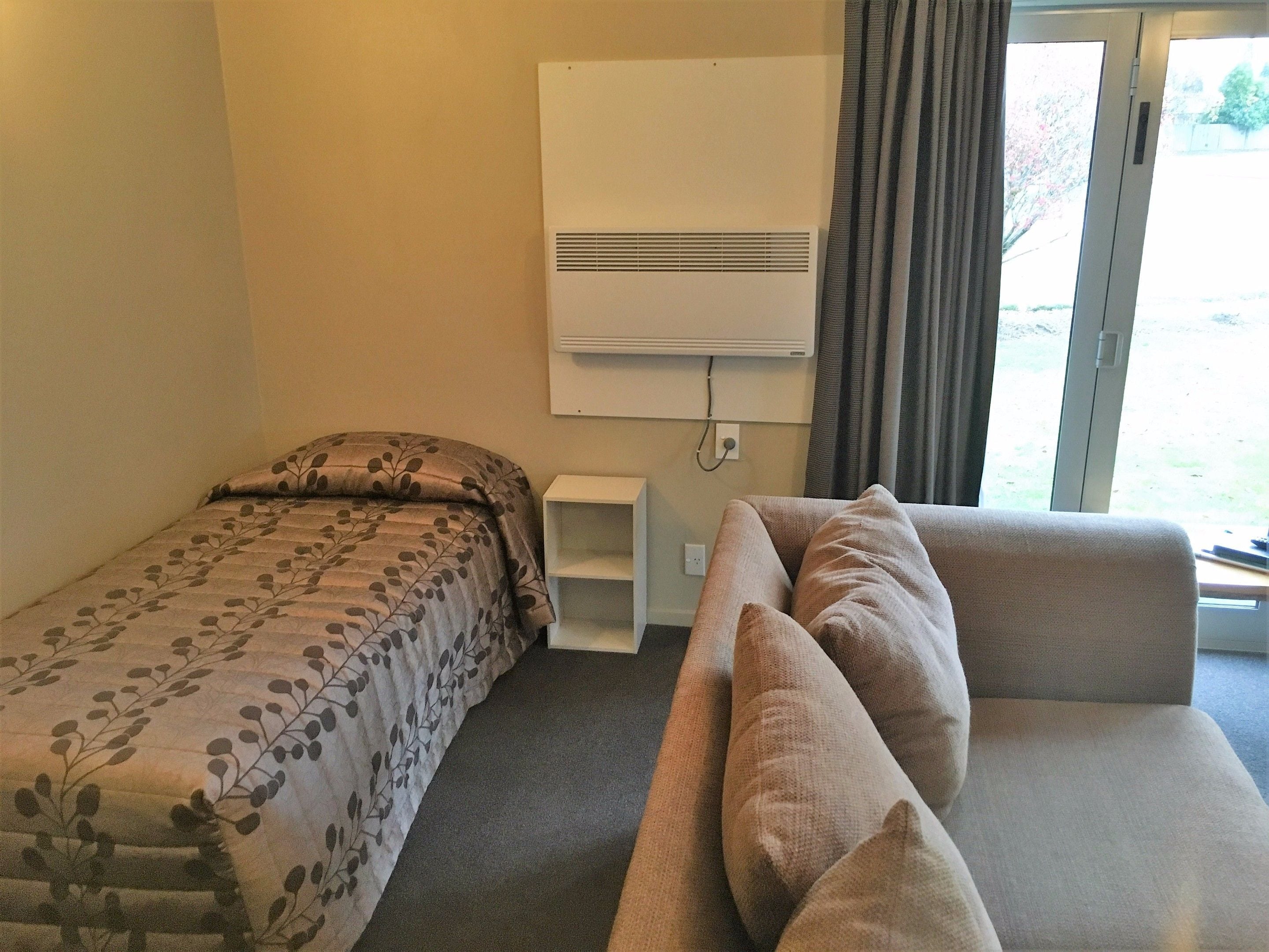 A room with a bed, a sofa, a wall-mounted air conditioner, and a window with curtains.