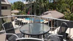 Una mesa redonda de vidrio con cuatro sillas, una piscina y palmeras al fondo.