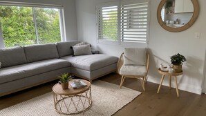Una sala moderna con un sofá seccional gris, una mesa de centro de mimbre redonda, un sillón de mimbre y una pequeña mesita auxiliar con una planta.