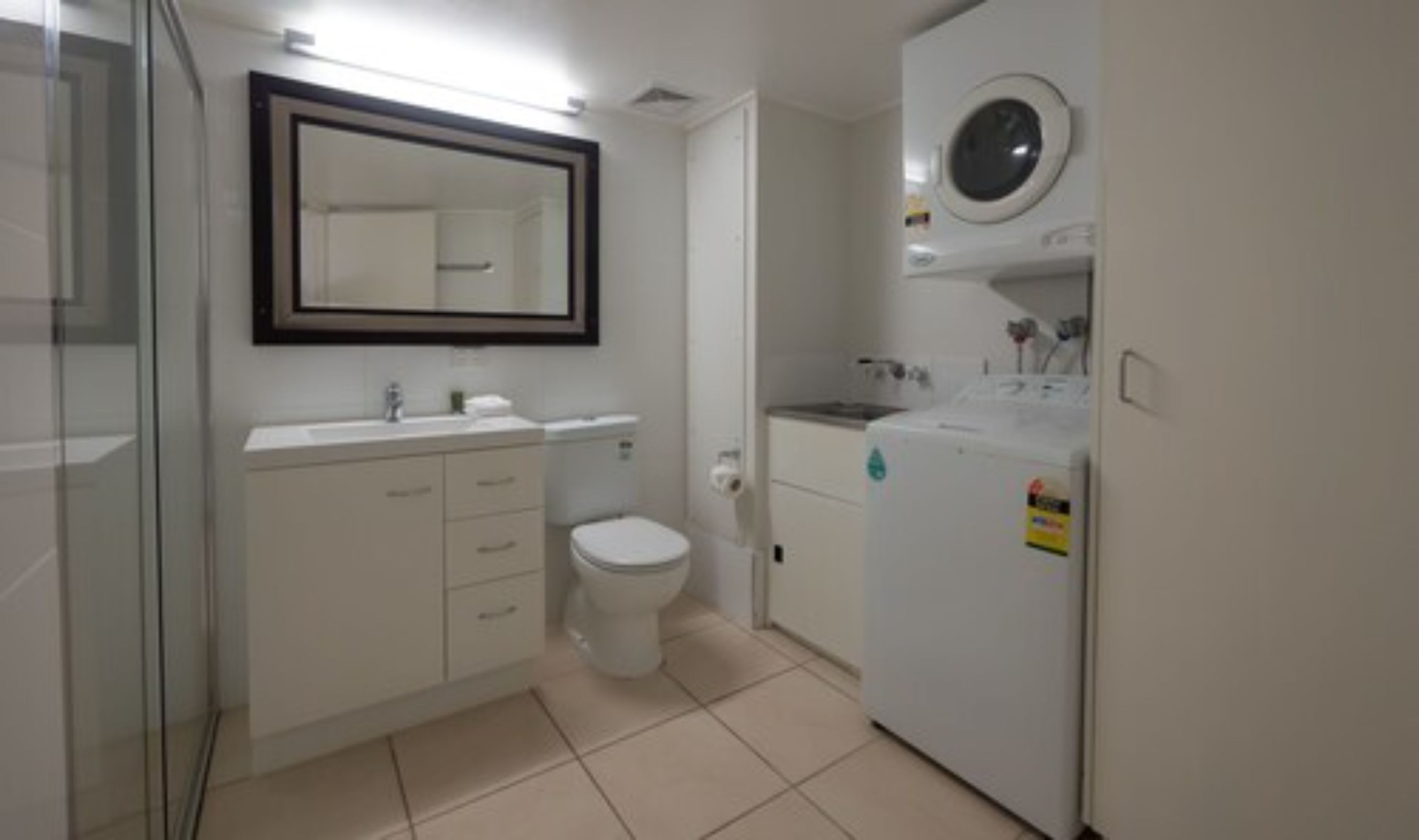A modern bathroom with a toilet, sink, mirror, and a washing machine.