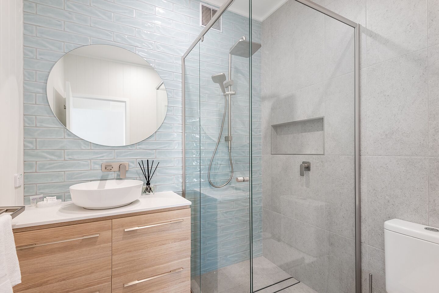 Une salle de bain moderne avec une douche à parois de verre, un miroir rond et un lavabo blanc.
