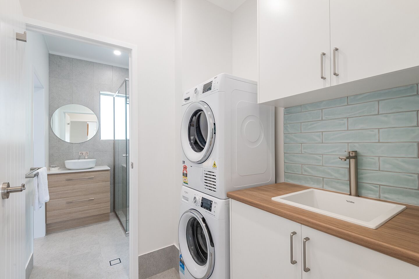 Une salle de bain moderne équipée d’un lave-linge double, d’un évier et d’un miroir.