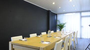 A conference room with a long wooden table, white chairs, and a potted plant.