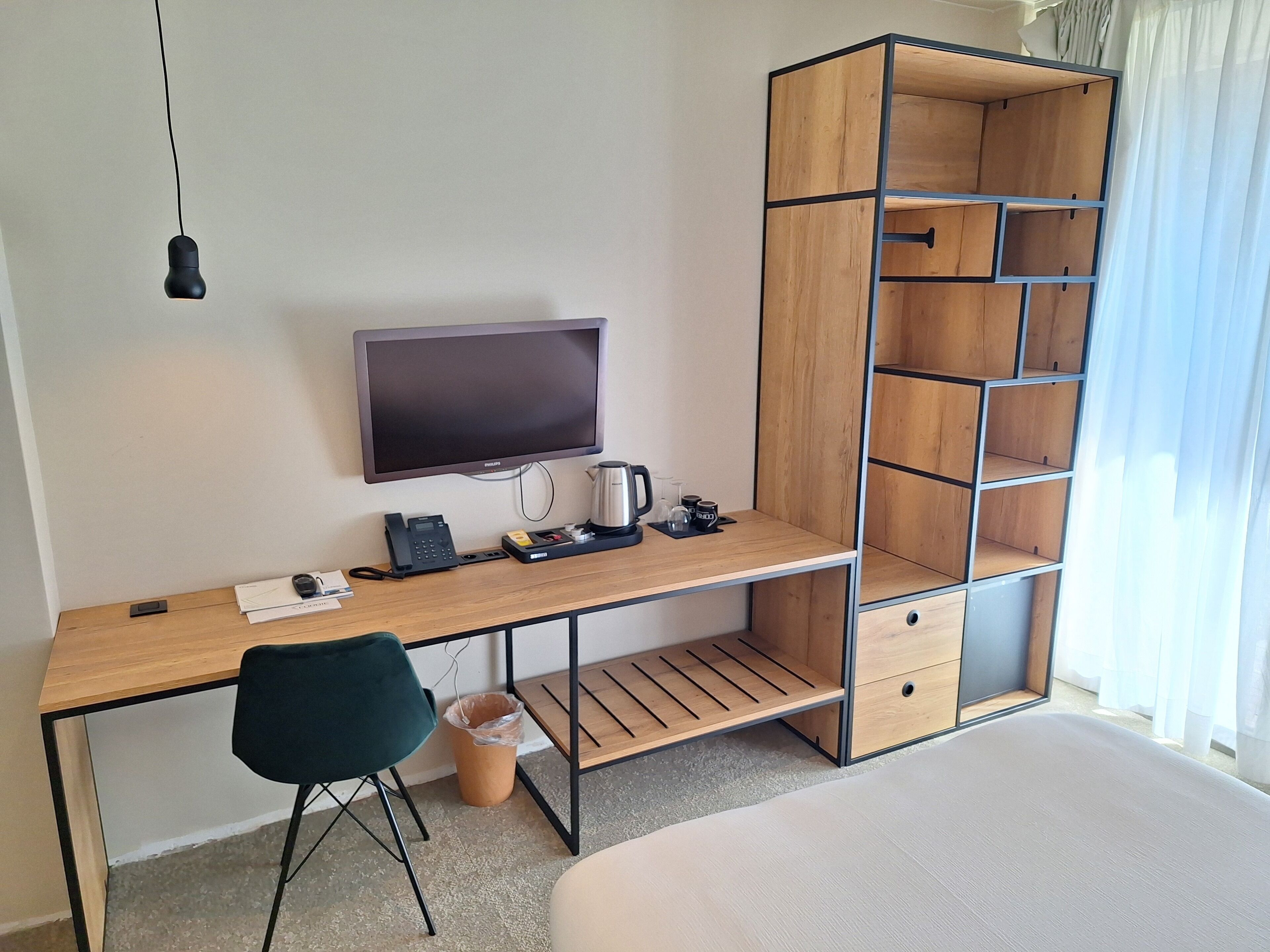 Una habitación de hotel moderna con un escritorio de madera, un televisor de pantalla plana, una cafetera y estanterías empotradas.