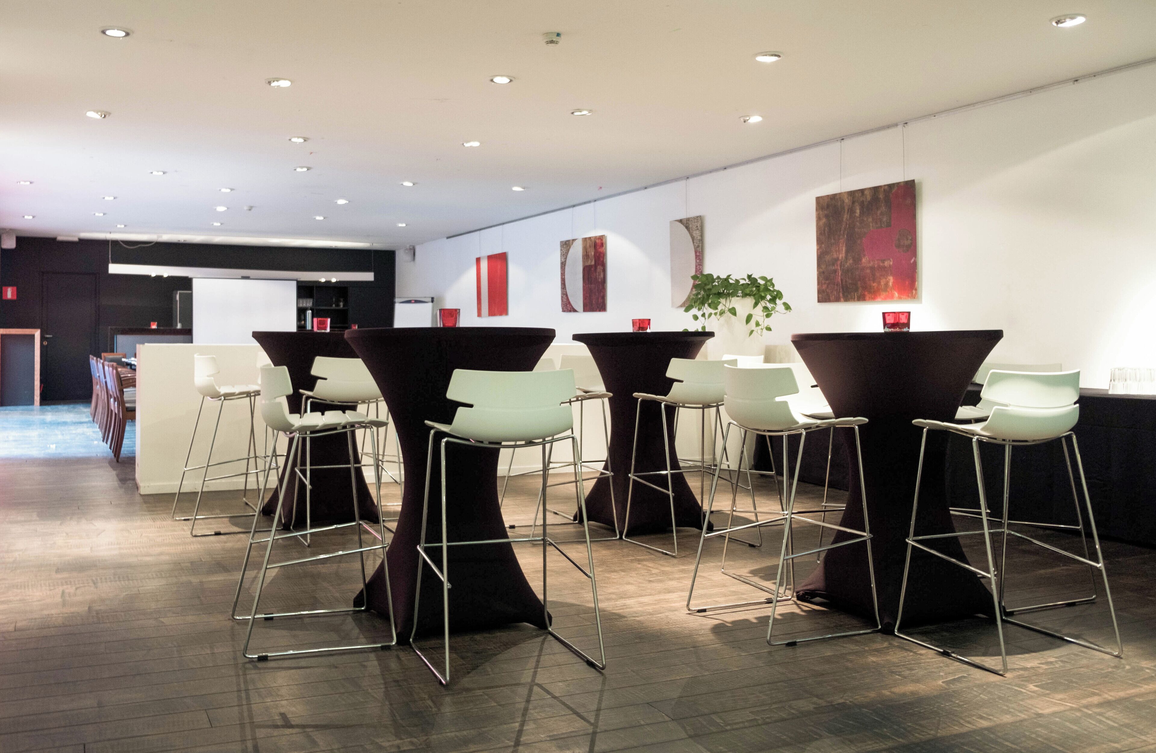A modern bar area with high stools and tables, a potted plant, and abstract wall art.