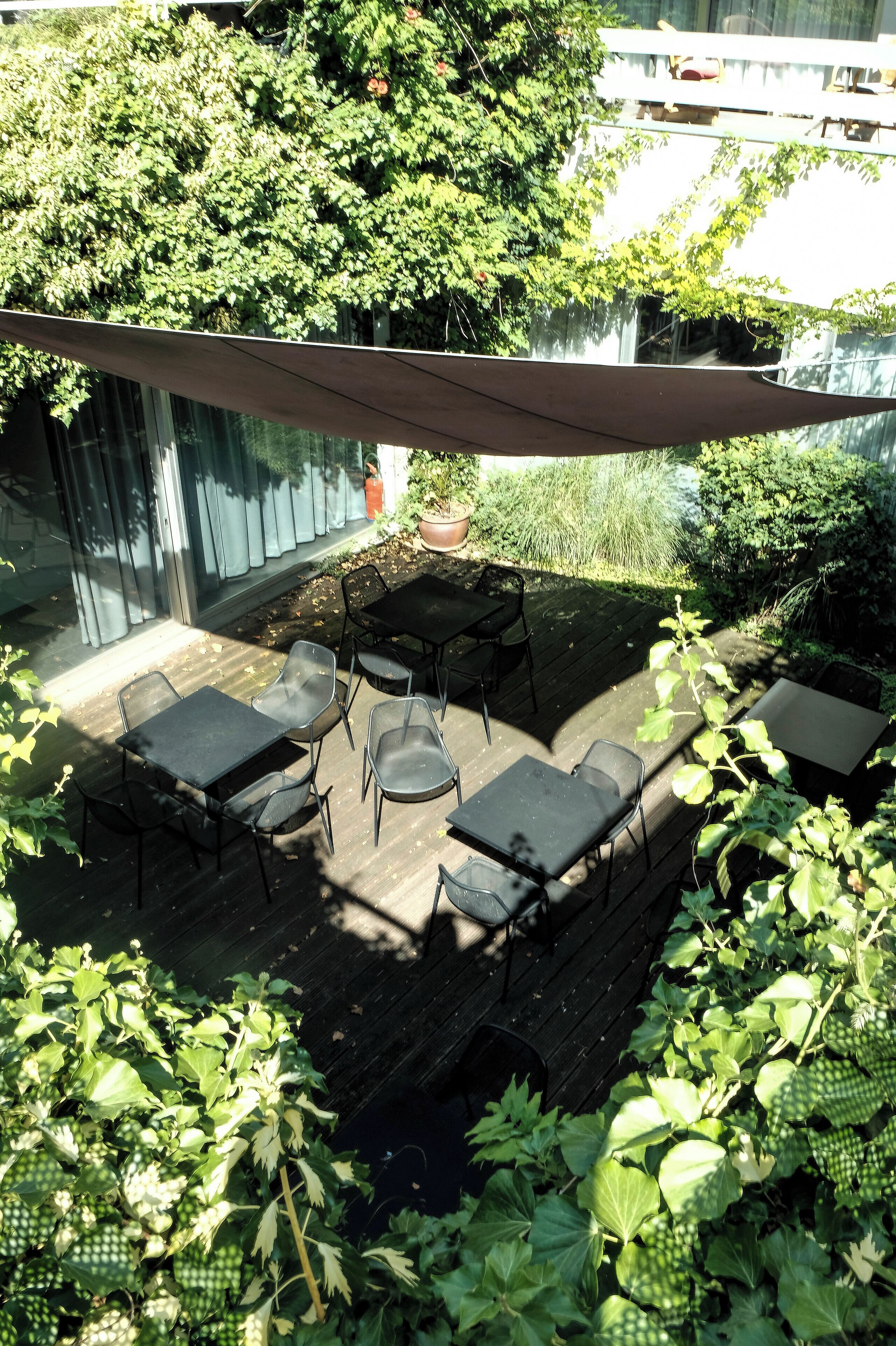 An outdoor patio with a table and chairs, surrounded by lush greenery and a shaded area.