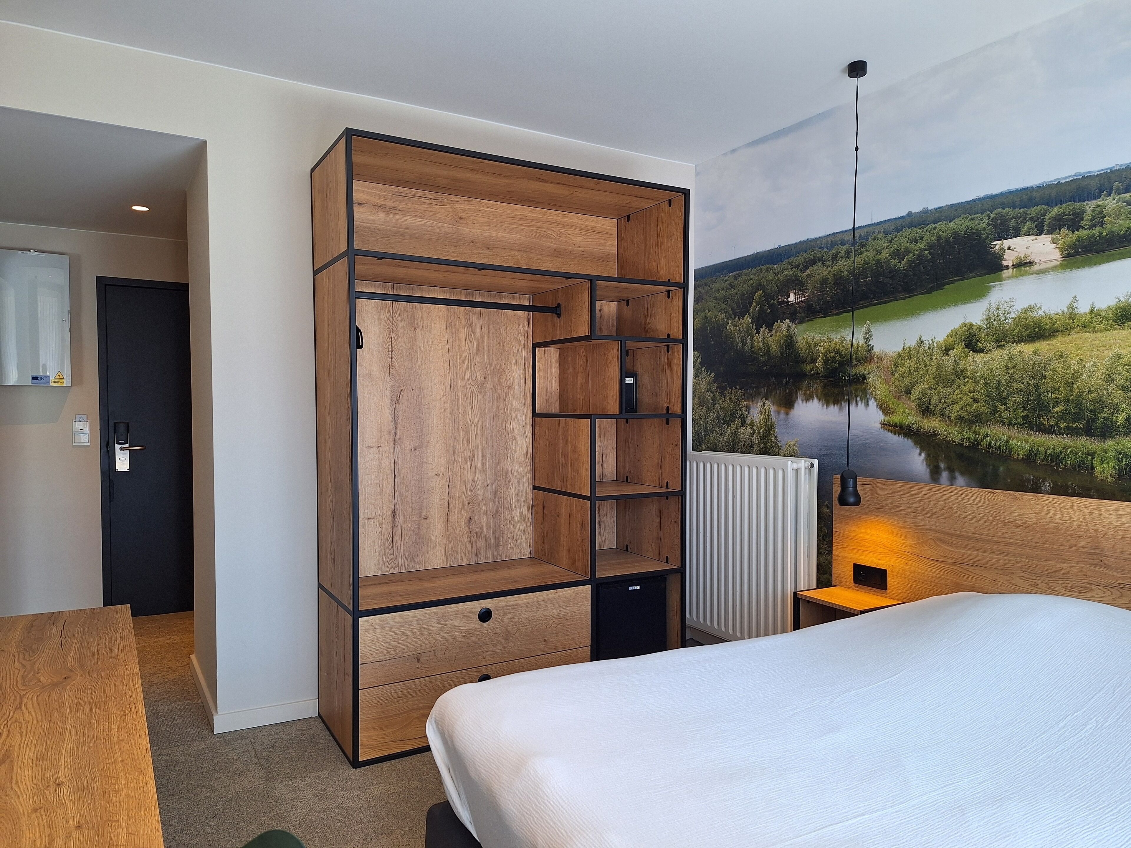Ein Hotelzimmer mit großem Holzschrank, einem Bett, einem Heizkörper und schöner Aussicht auf See und Wald.
