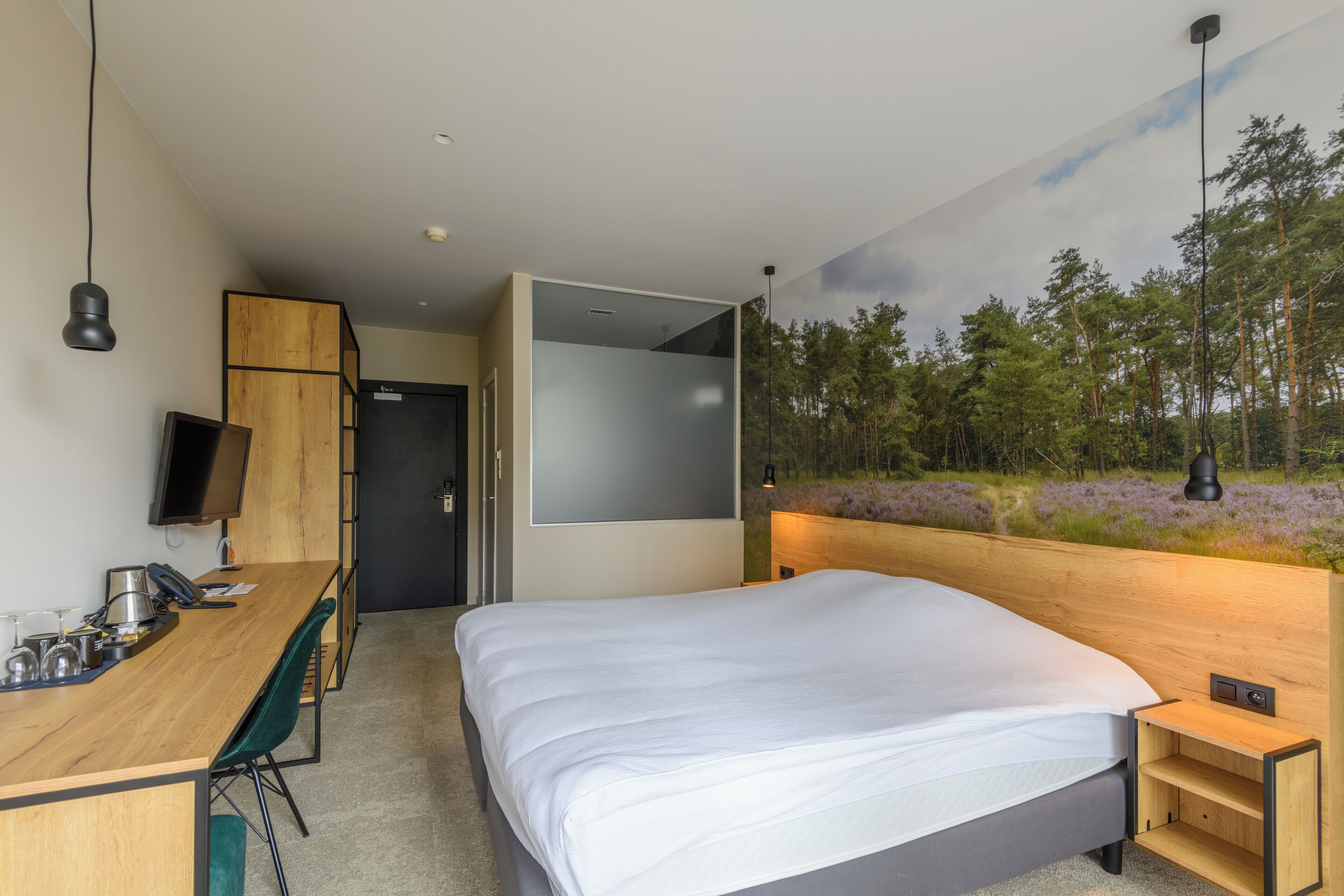 A modern hotel room with a bed, desk, chair, and a TV.