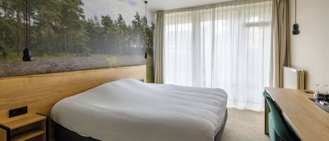 Un dormitorio con una cama grande, un escritorio de madera y vistas a un bosque a través de cortinas traslúcidas.