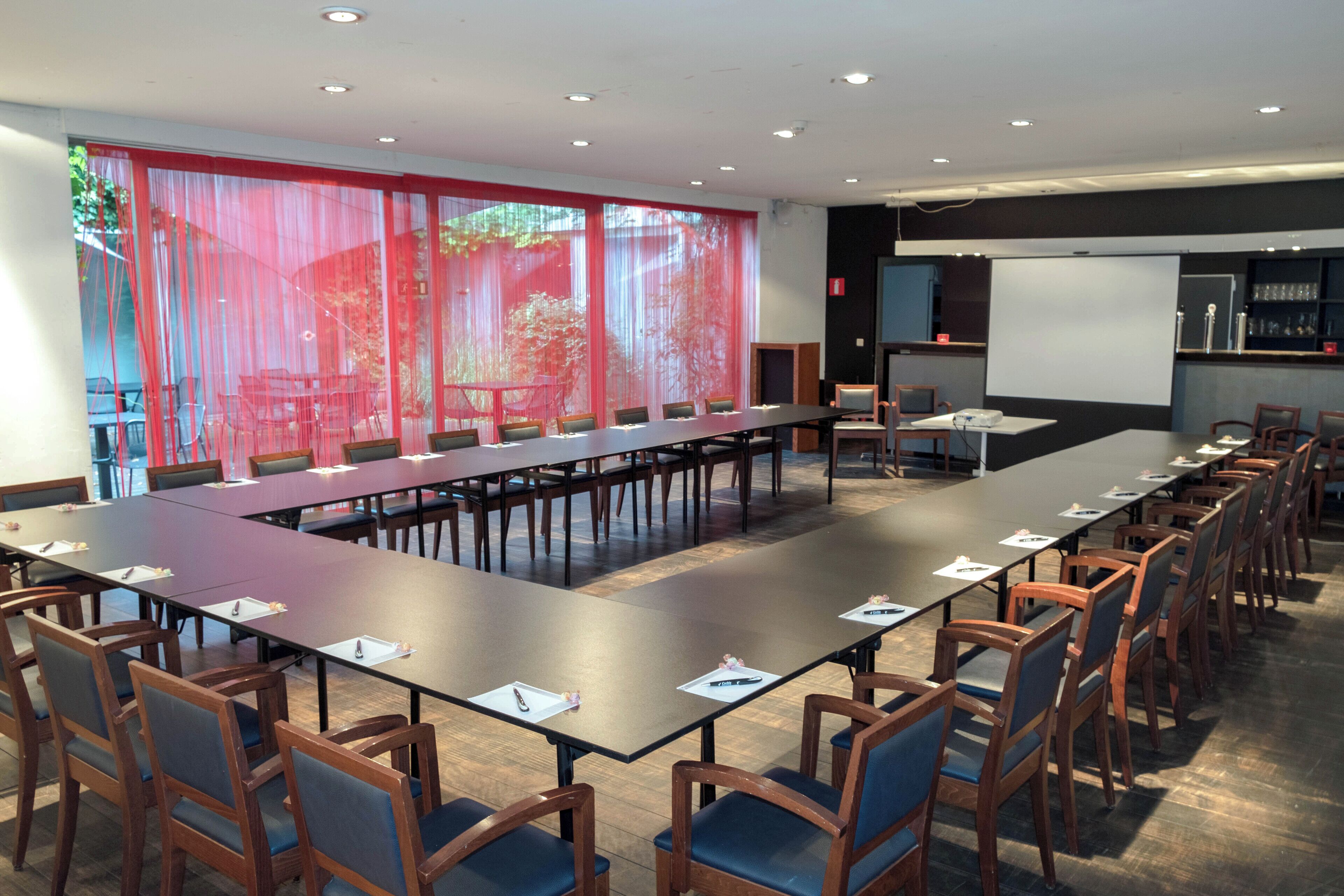 A conference room with a long table, chairs, a projector screen, and a screen for presentations.