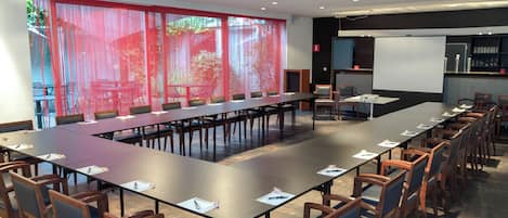 A conference room with a long table, chairs, a projector screen, and a screen for presentations.