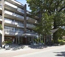 A multi-story hotel with a modern architectural design, featuring a covered entrance with glass doors and outdoor seating.