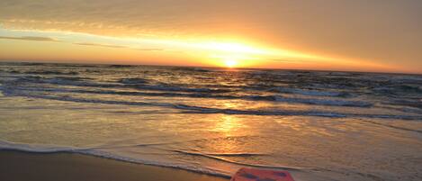 Un atardecer sobre el océano con una tabla de surf en la playa.