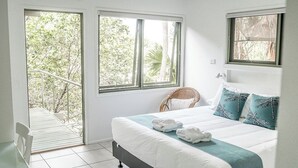 Une chambre à coucher avec un lit, deux fenêtres, une chaise et un balcon.