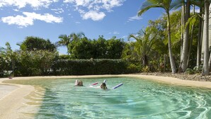 Une piscine aux eaux cristallines, bordée d’une plage de sable et de palmiers.