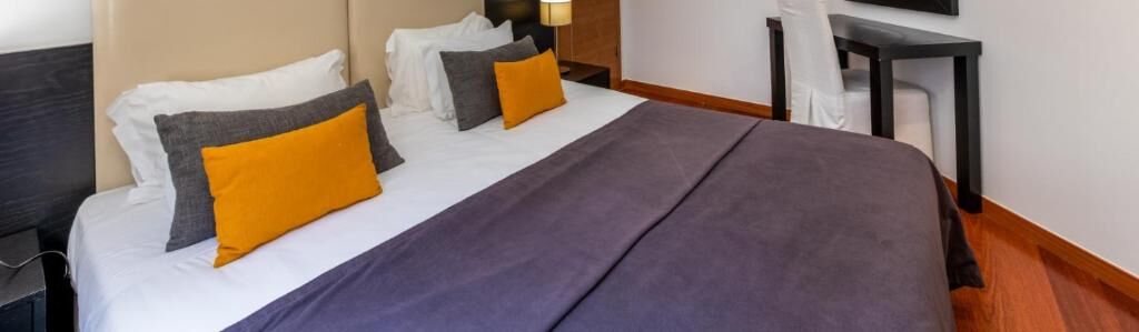 A hotel room with a bed, a nightstand, a lamp, and a chair.