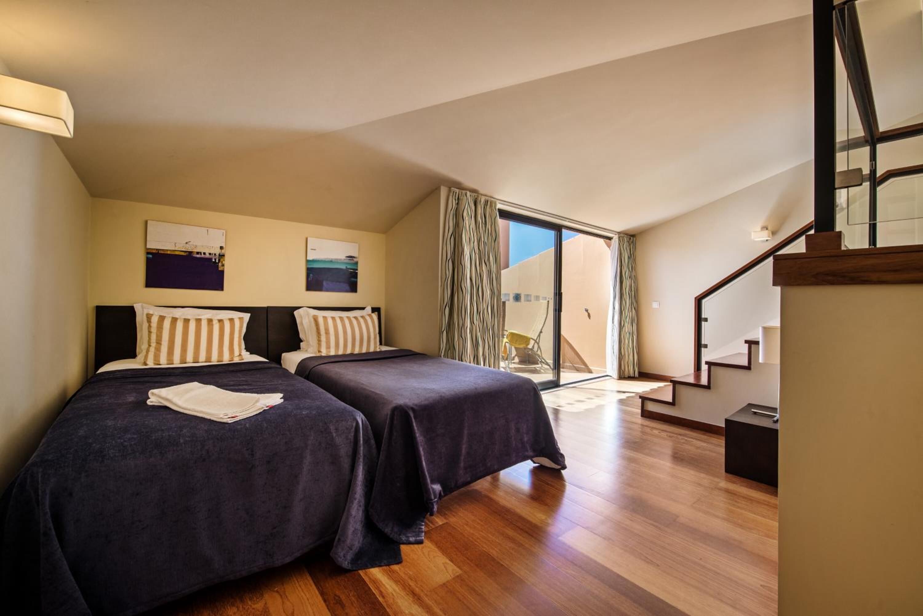 A bedroom with two beds, a staircase, and a view of the outdoors.