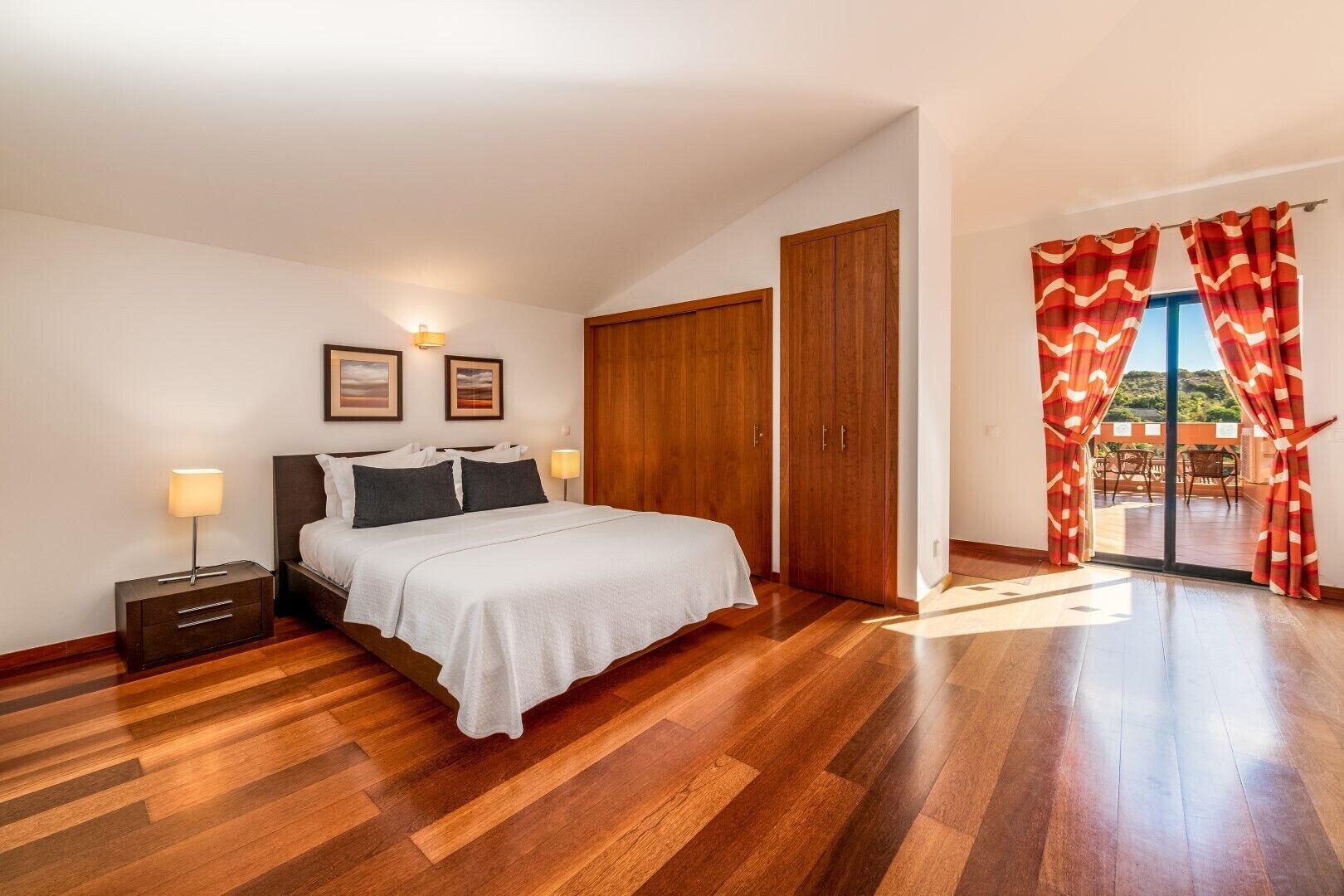 A bedroom with a bed, bedside tables, a wardrobe, and a balcony with curtains.
