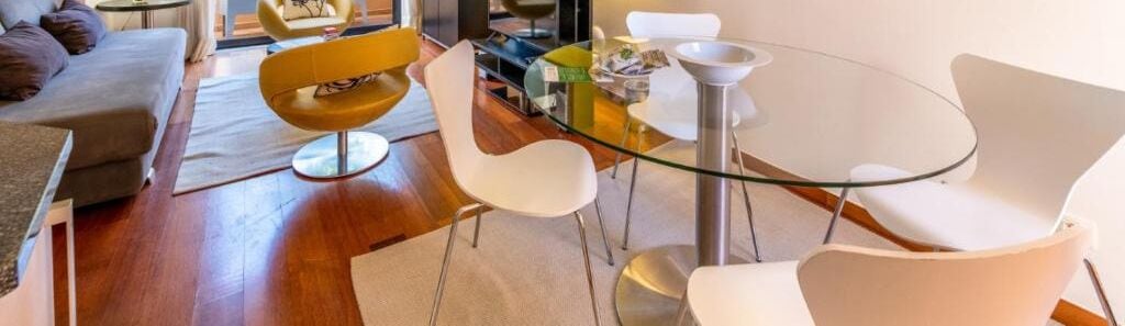 Un salon moderne avec une table à manger à plateau de verre, entourée de chaises blanches, d’un canapé et d’un fauteuil jaune.