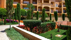 A hotel with multiple balconies, a well-maintained garden with various shrubs and flowers, and a clear sky. - Baia da Luz (Lagos)