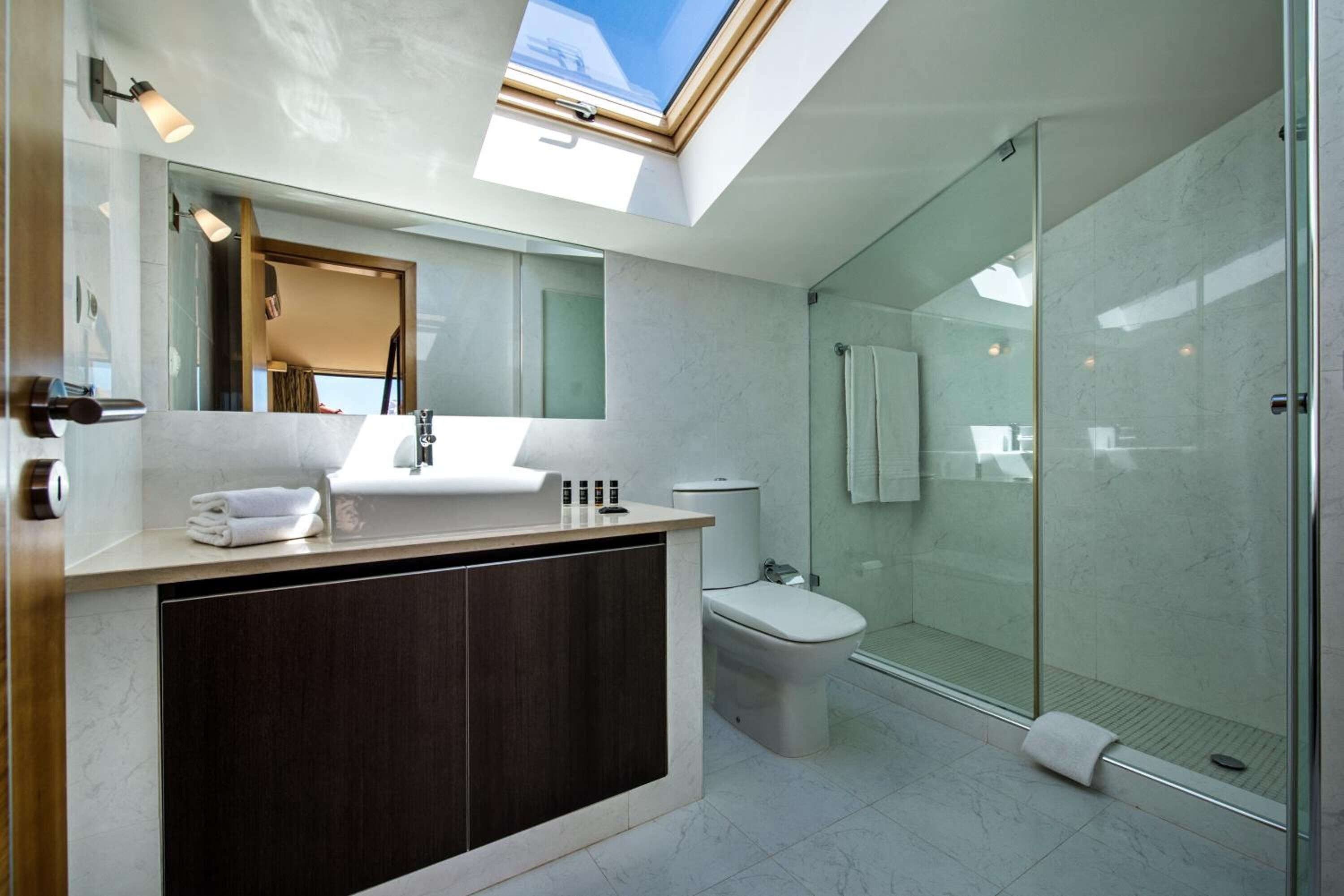A modern bathroom with a skylight, a glass shower enclosure, and a dark wood vanity.