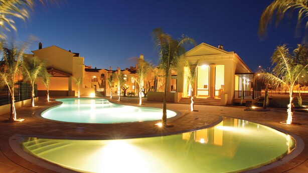 A swimming pool area with two pools, palm trees, and buildings at dusk. - Baia da Luz (Lagos)
