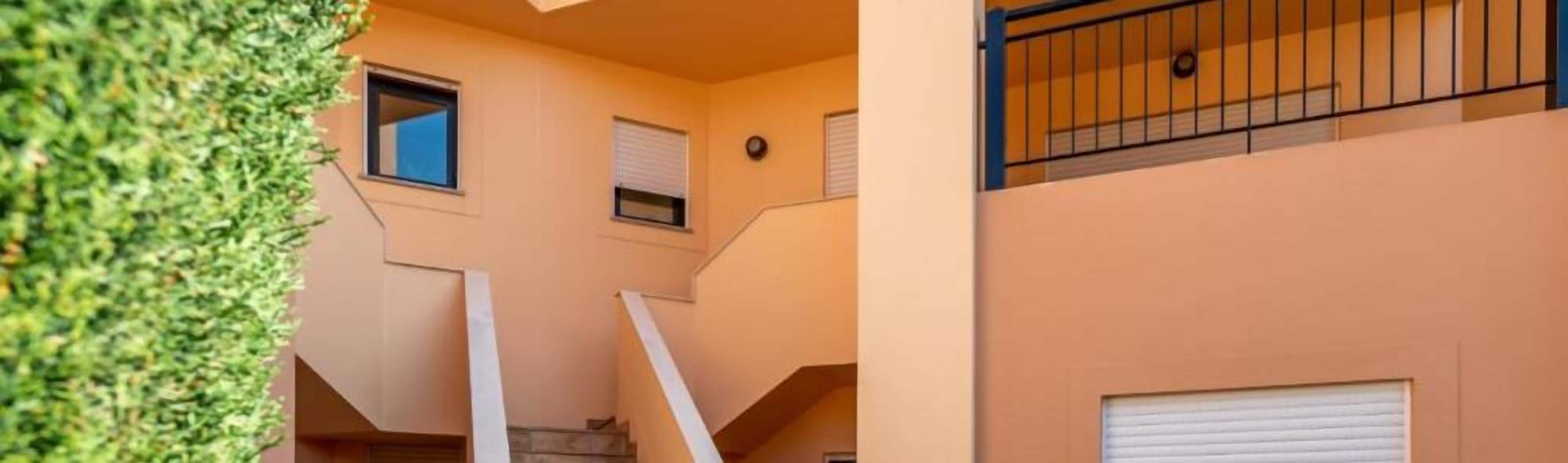 A multi-level residential building with a beige exterior, a visible staircase, and a balcony with a metal railing.