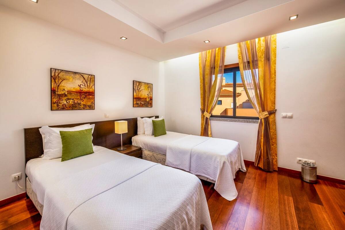 A hotel room with two beds, a window with curtains, and artwork on the walls.