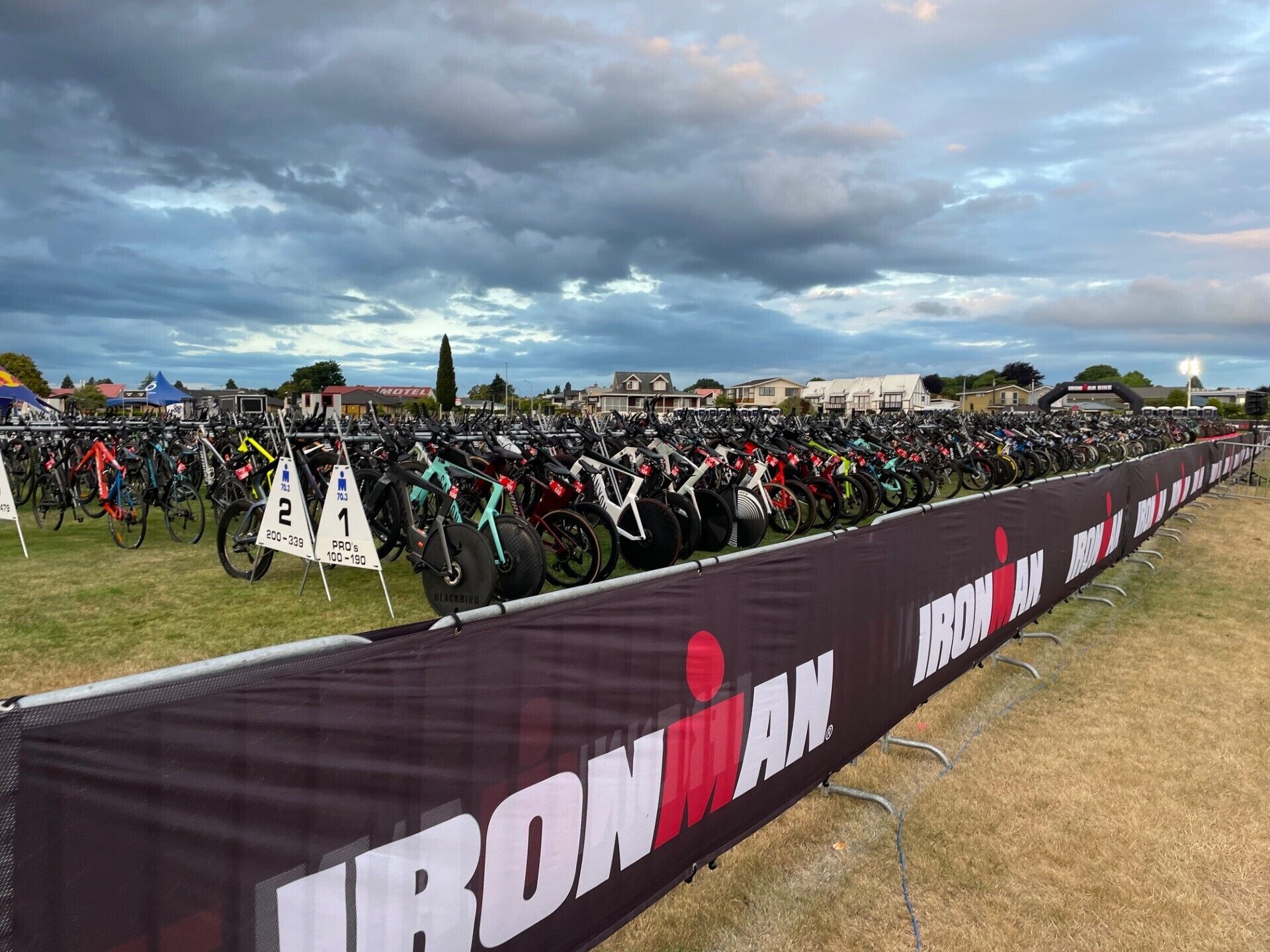 A large outdoor area with rows of bicycles lined up against a backdrop of buildings and a cloudy sky.