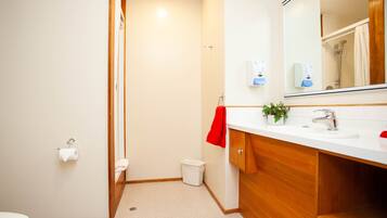 A modern bathroom with a wooden vanity, a white sink, a mirror, and a shower area.