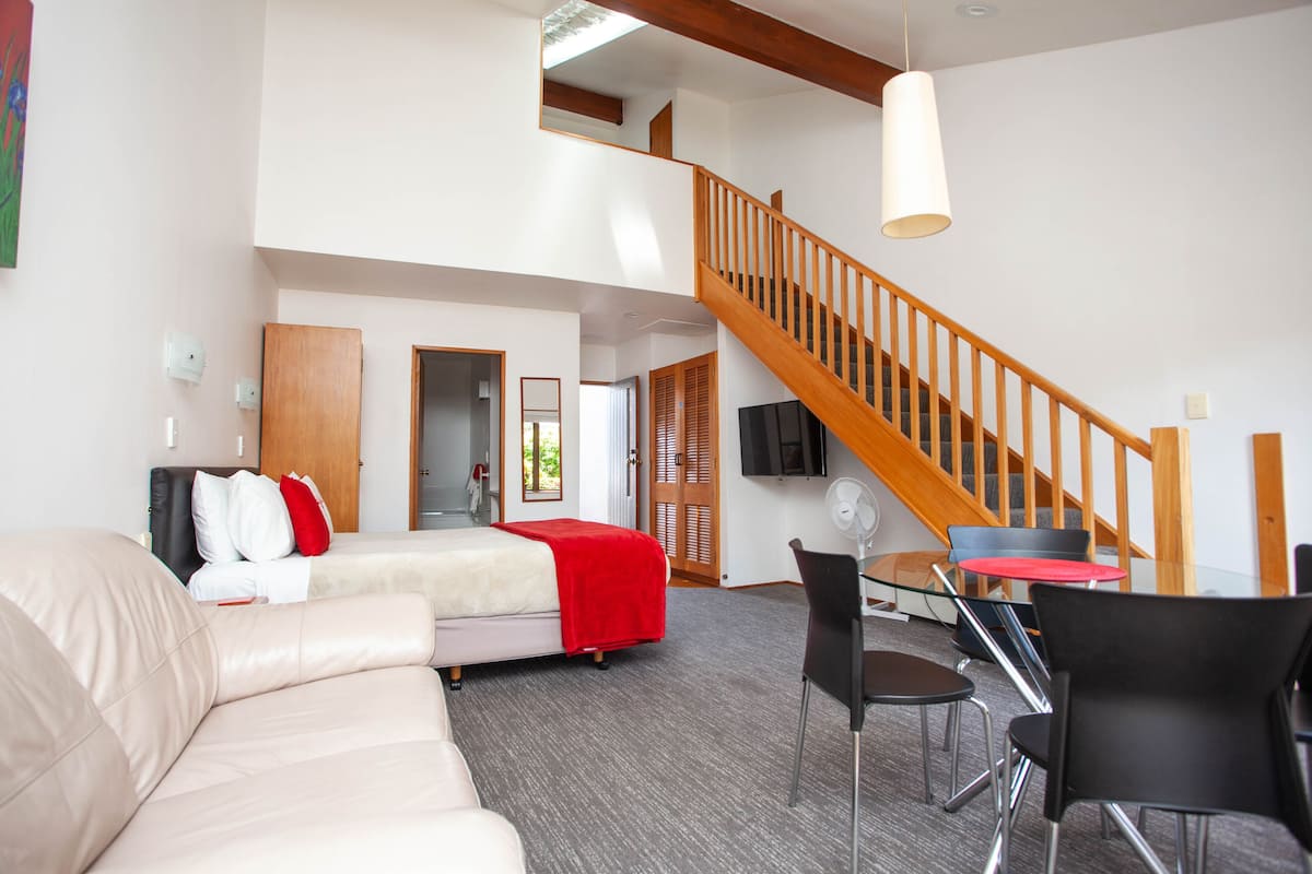 Un vaste espace de vie comprenant un grand lit, un canapé, une table à manger avec des chaises et un escalier menant à un niveau supérieur.