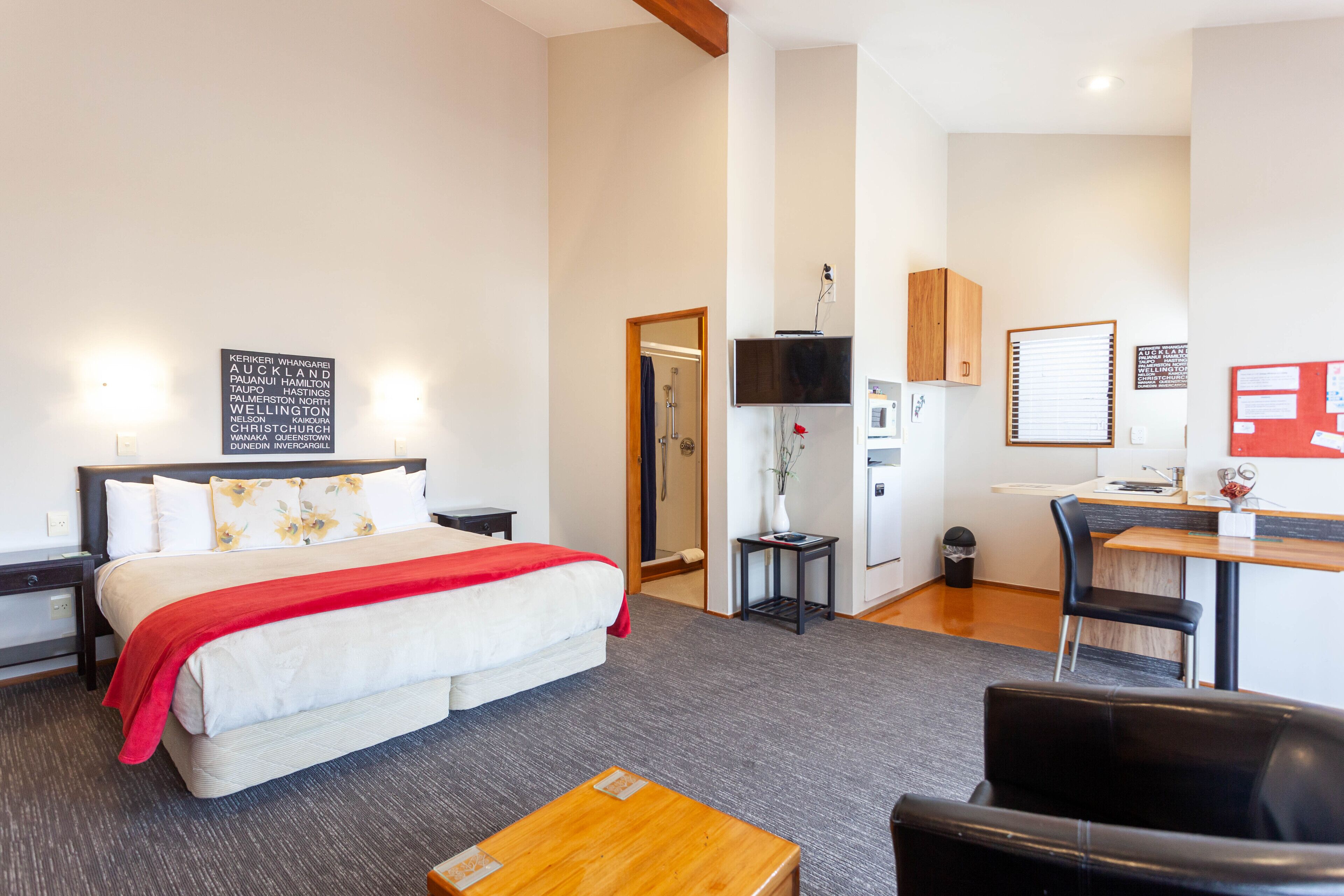 A modern hotel room with a large bed, a desk, a chair, and a small table.