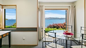 A room with a glass table and chairs, a view of the sea, and a window with curtains. - Cascades Lakefront Motel (Taupo)
