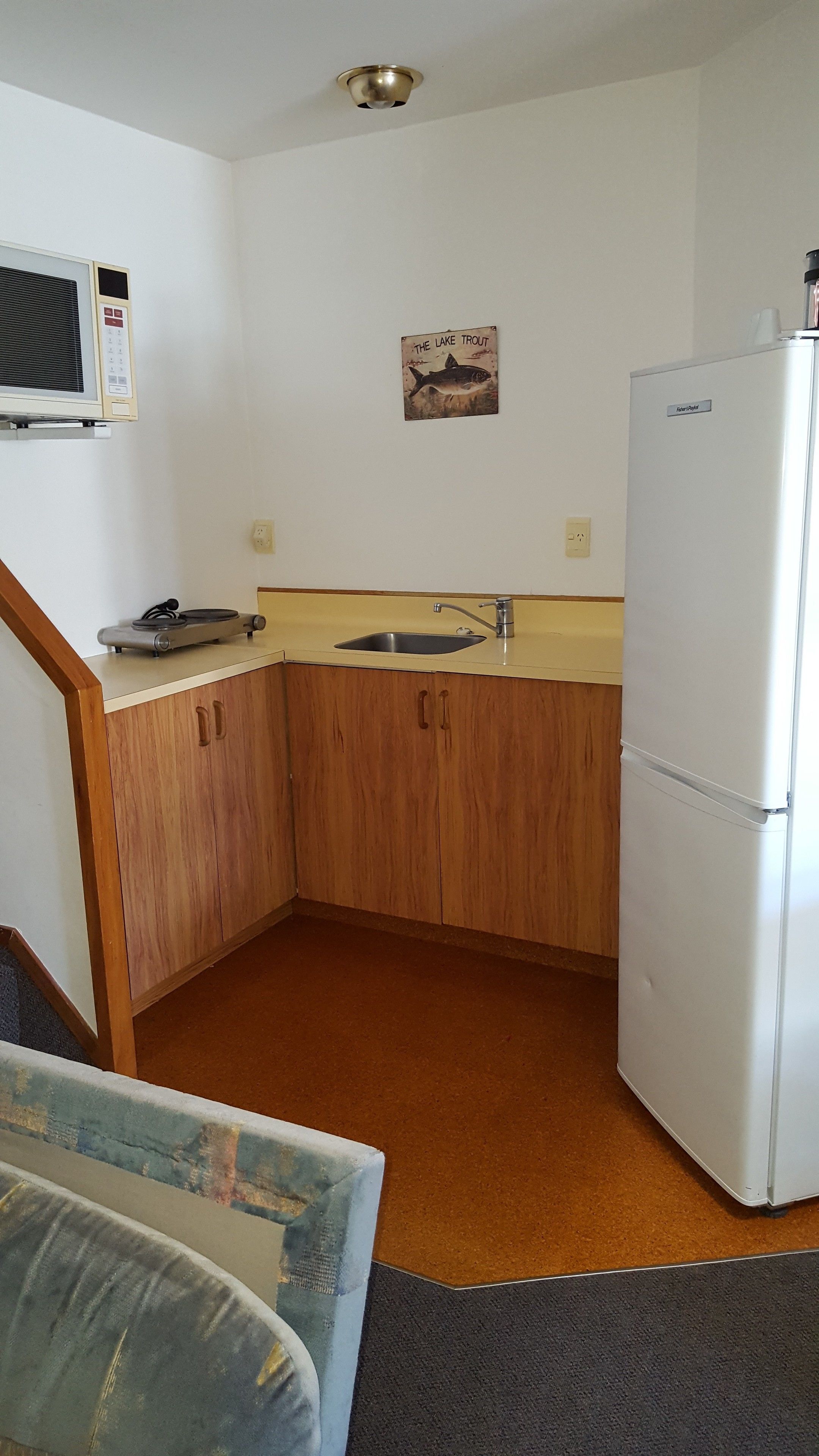 A compact kitchen with wooden cabinets, a sink, a refrigerator, and a wall-mounted microwave.