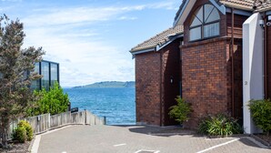 A waterfront property with a paved driveway leading to a brick building with a large window and a door. - Cascades Lakefront Motel (Taupo)