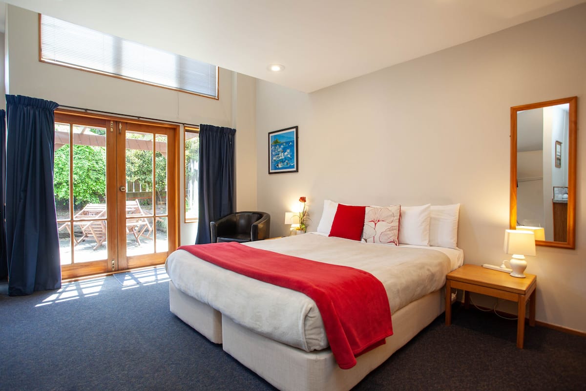 Une chambre d’hôtel avec un grand lit, une table de chevet avec une lampe, une chaise et une vue sur l’extérieur grâce à une porte-fenêtre coulissante.